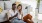 a man and woman with take out, sit against a couch on their living room floor and watch at their cell phone